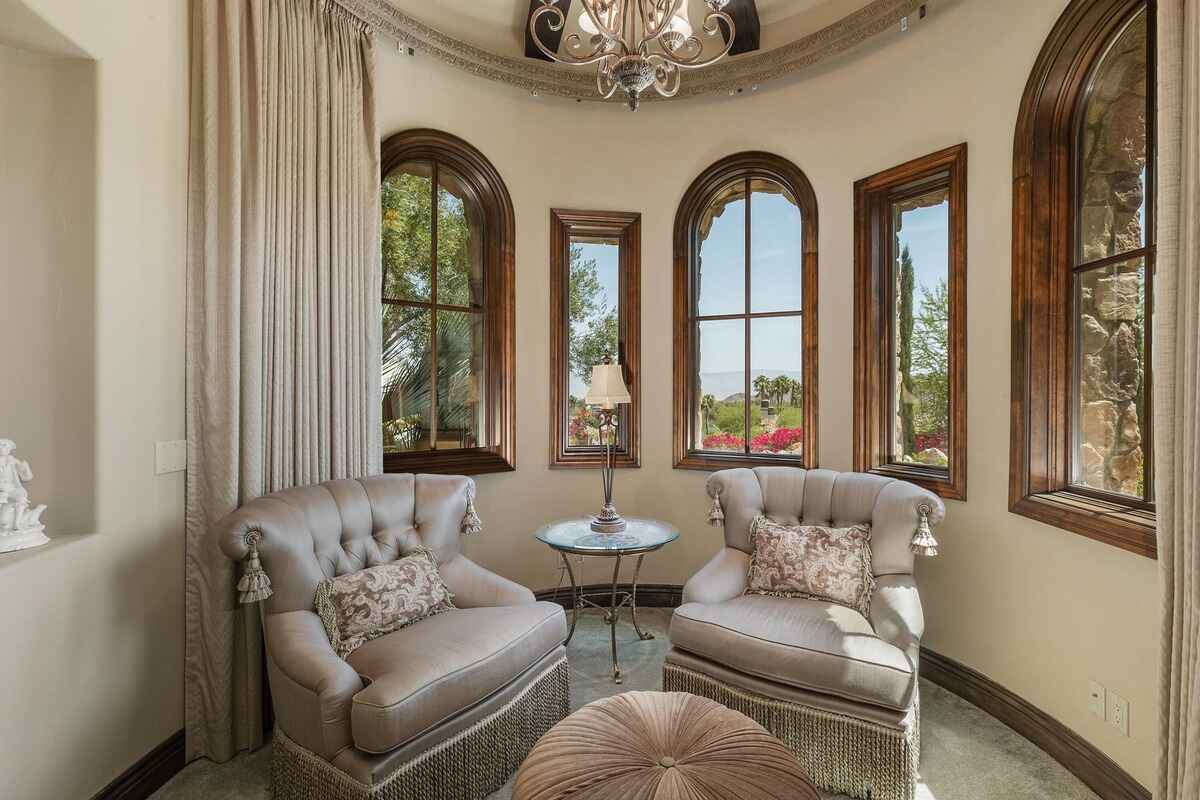 Sitting area in a circular room with upholstered chairs, tall windows, and detailed molding.