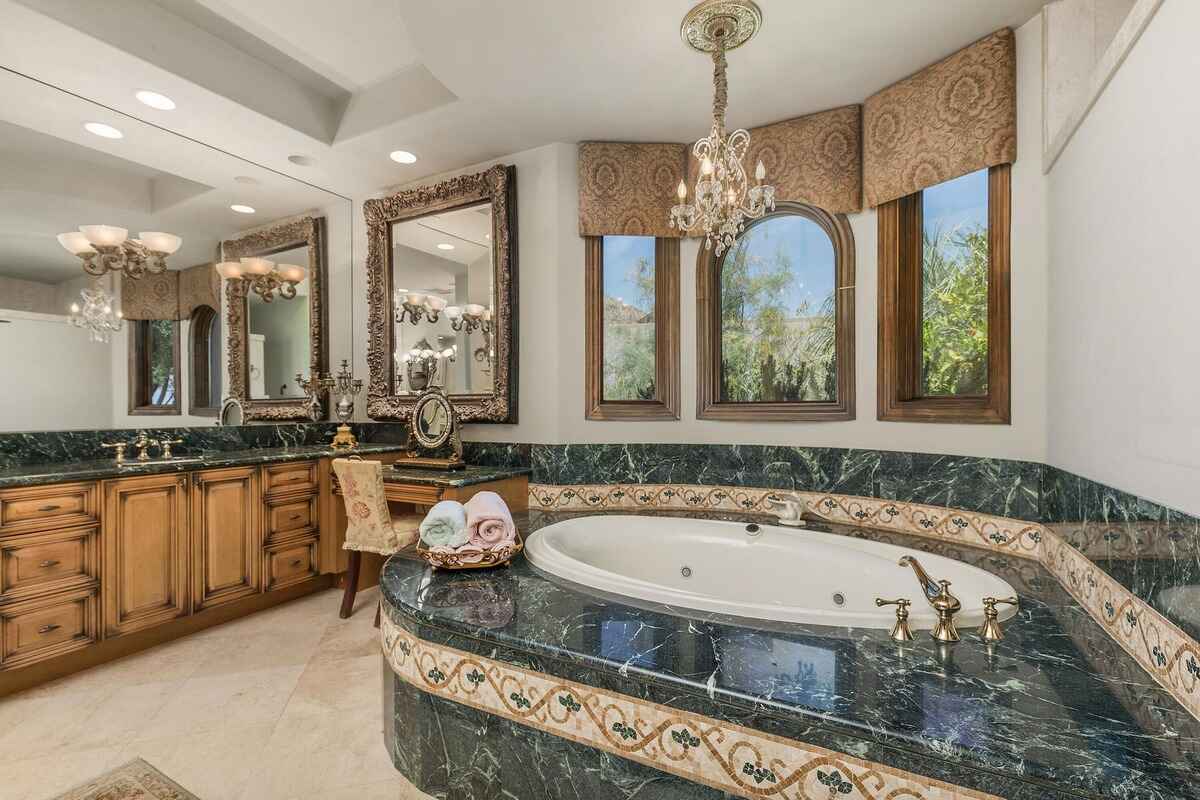 Bathroom showcasing a green marble bathtub, wooden cabinetry, and decorative mirrors.