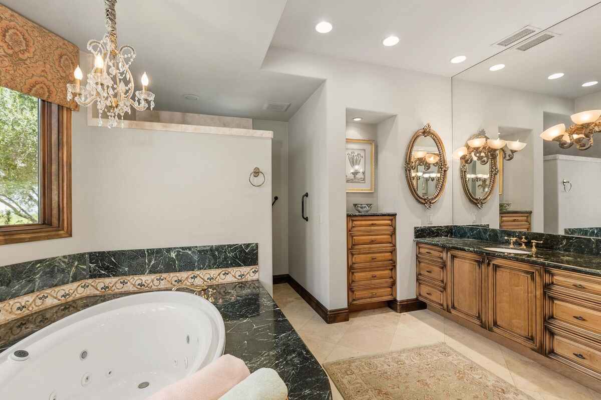 Additional view of the bathroom with dual sinks, marble accents, and ornate chandeliers.