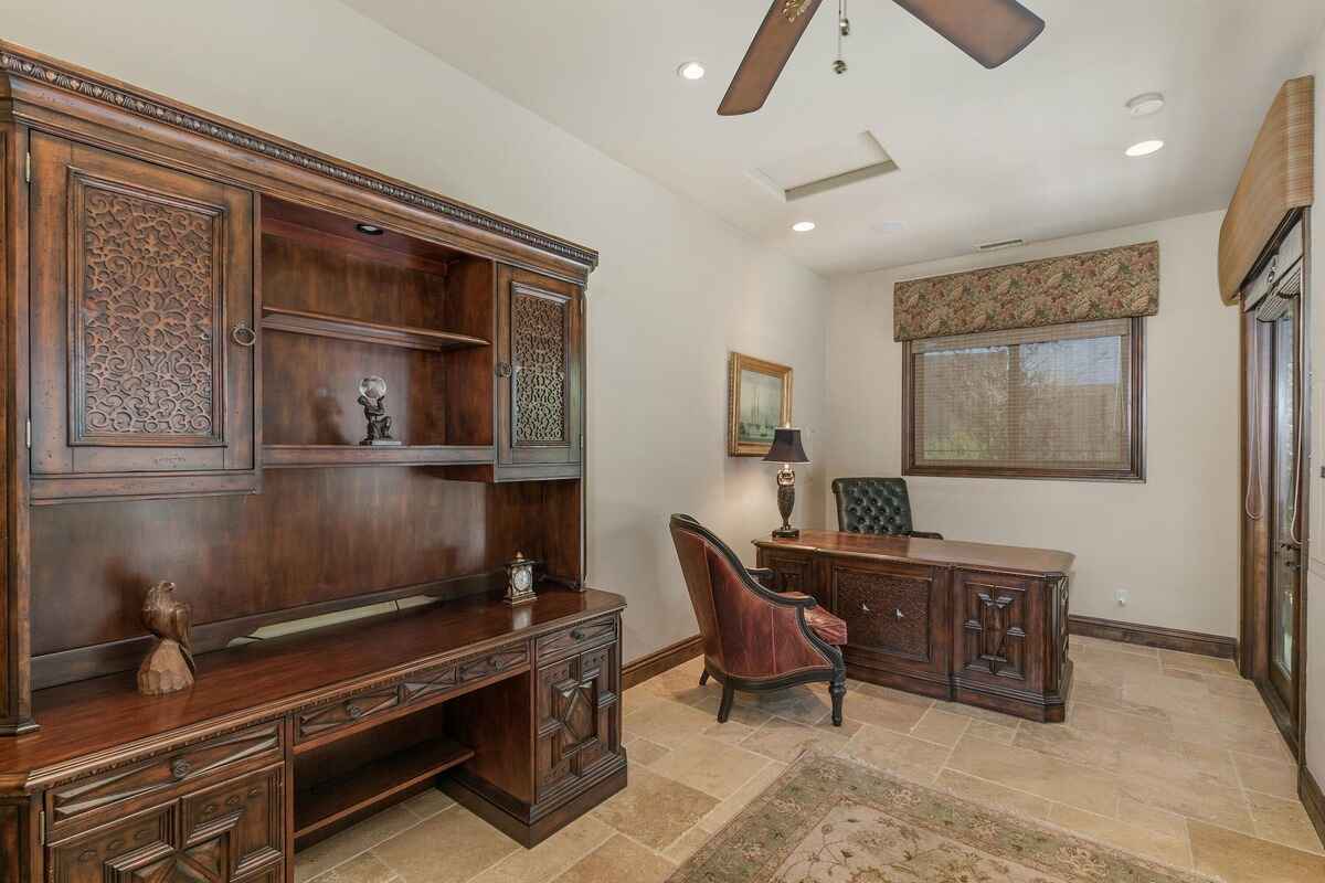 Office space with wooden furniture, a desk, and bookshelves under soft natural lighting.