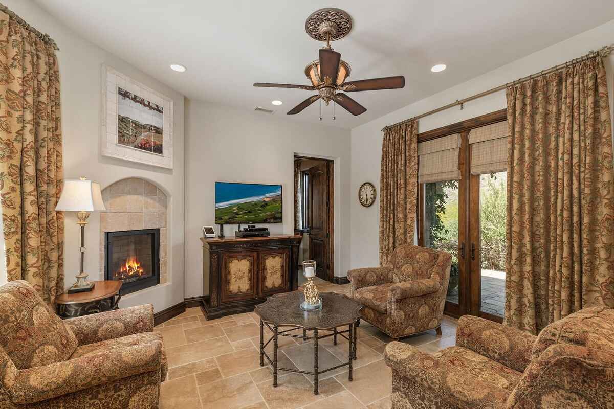 Cozy living area with a fireplace, patterned curtains, and a ceiling fan.