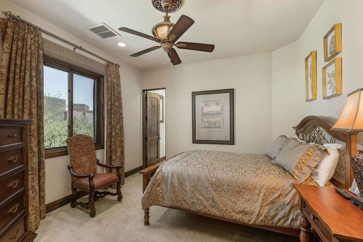 Bedroom with a ceiling fan, ornate furniture, and draped windows overlooking the outdoor greenery.