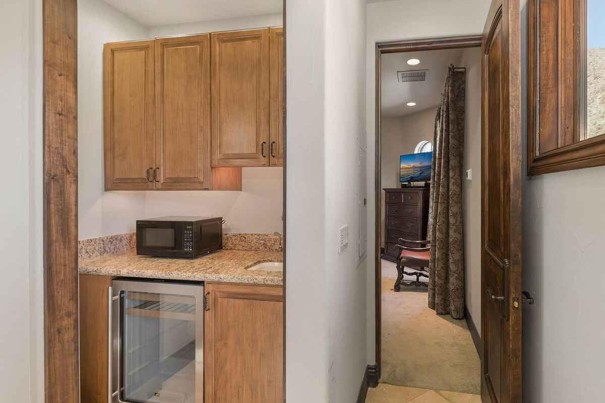 Compact kitchenette area with wooden cabinets, granite countertops, and a mini fridge next to a hallway.