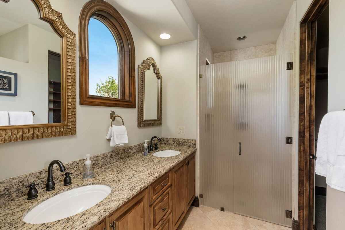 Bathroom featuring a double sink vanity with granite countertops and a walk-in shower with frosted glass.