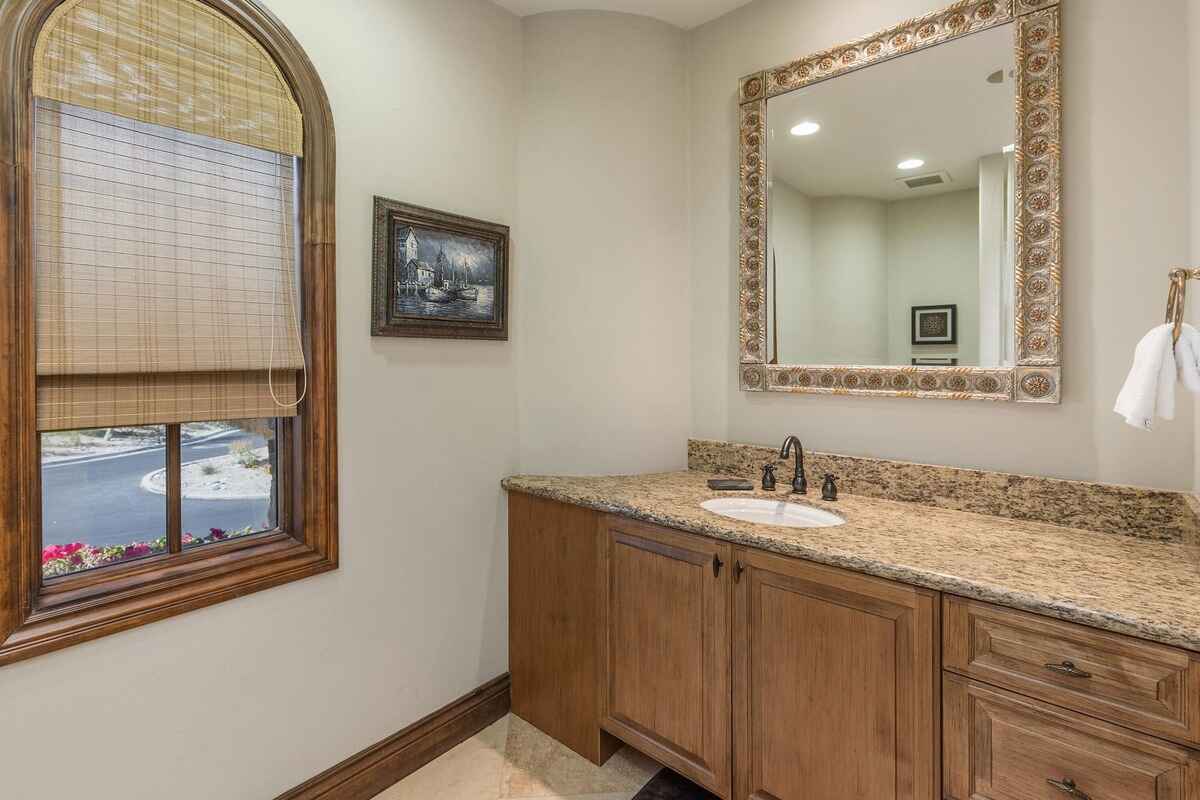 Powder room with a single sink vanity, granite countertop, and a large decorative mirror under soft lighting.