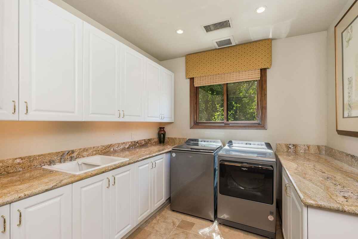 Laundry room equipped with white cabinetry, granite countertops, and modern washer and dryer units.