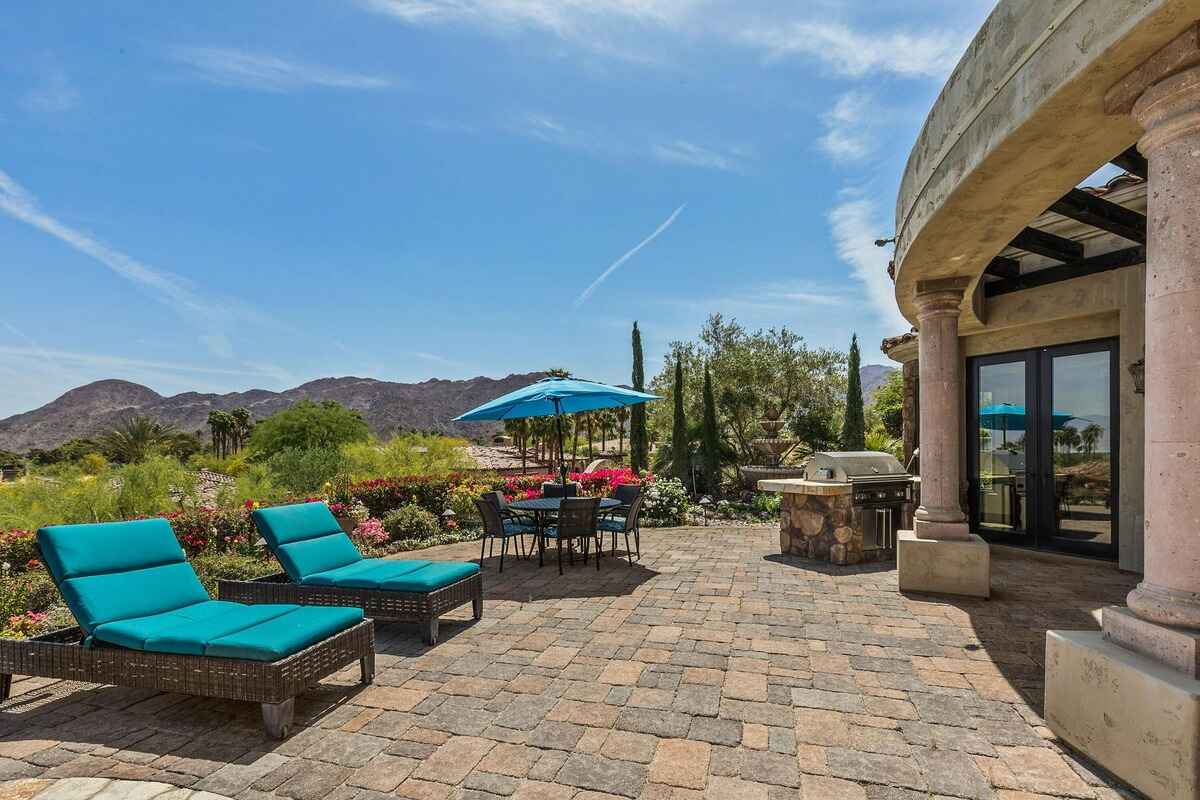 Outdoor seating area with loungers, a dining setup, and a barbecue station surrounded by vibrant landscaping.