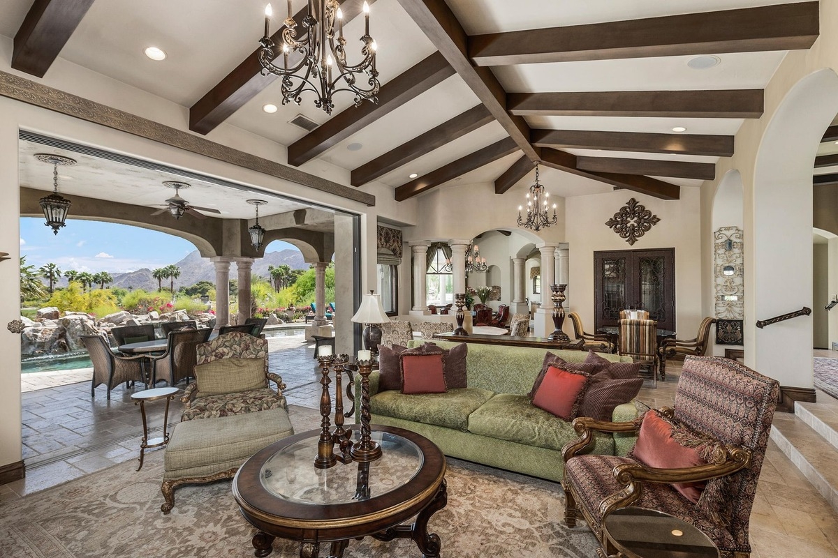 Living room featuring wood-beamed ceilings, chandeliers, and open layout leading to patio.