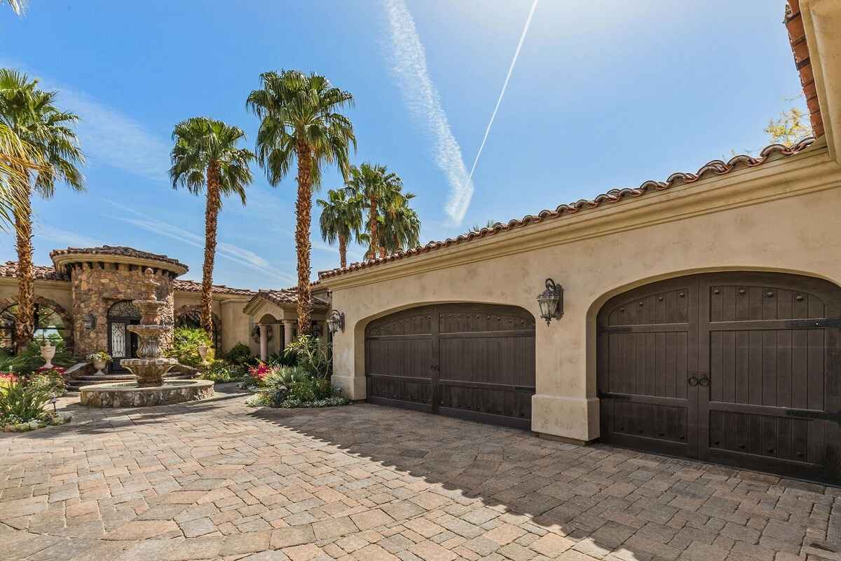 Spacious driveway and garage facade complementing the home's architectural design with palm trees lining the background.