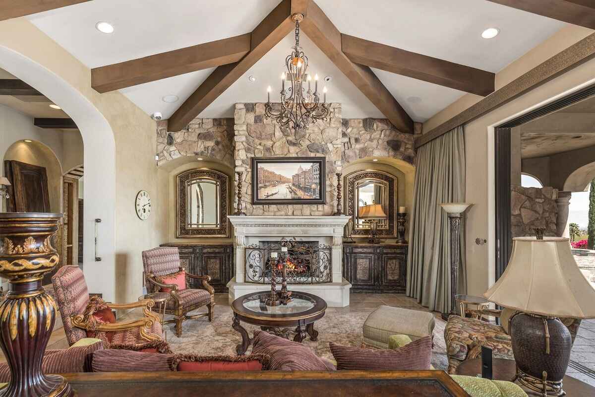 Cozy sitting area with stone fireplace, decorative mirrors, and chandelier beneath vaulted ceilings.