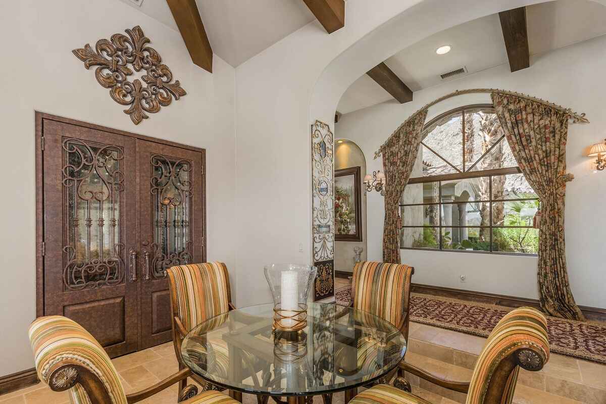 Small dining nook with striped chairs, glass table, and decorative wrought iron doors.