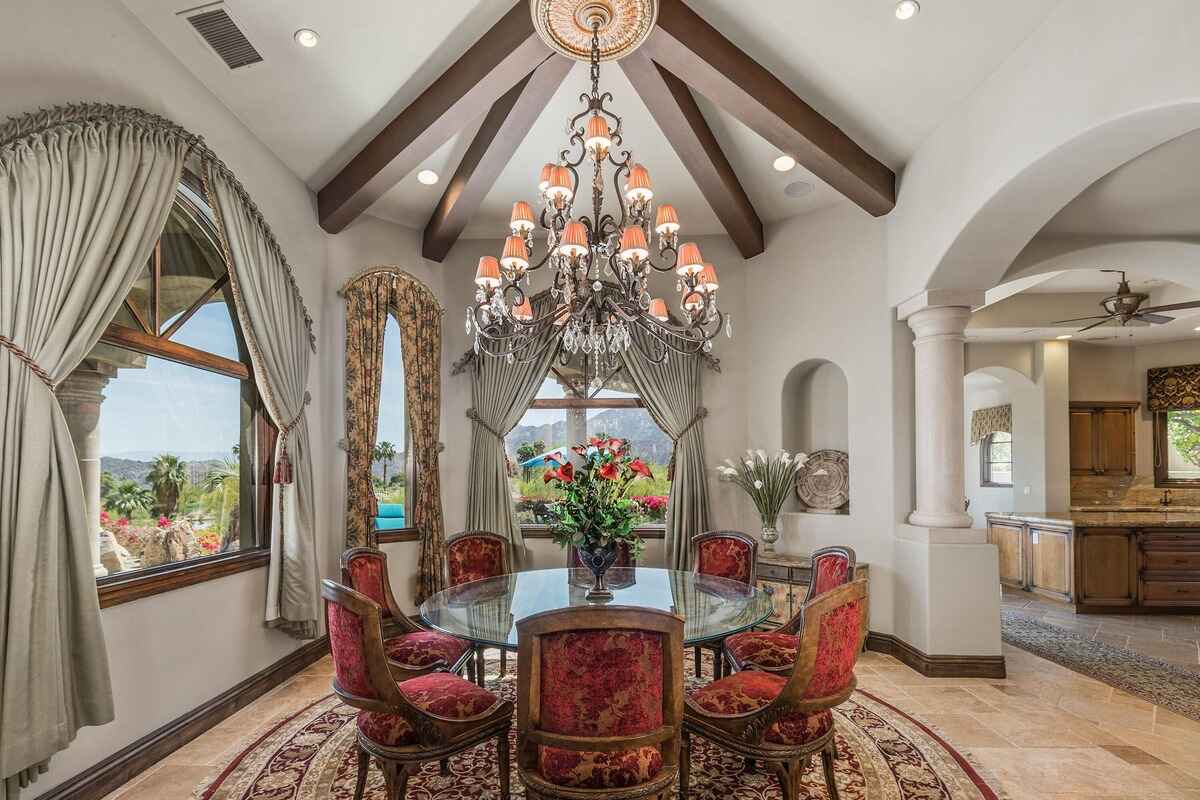 Formal dining room with vaulted ceilings, large windows, and elaborate chandelier above circular table.