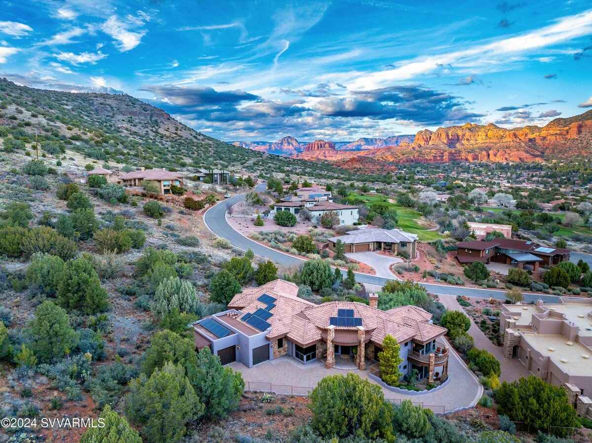 Aerial view of a large house surrounded by desert vegetation and hills, with red rock formations in the distance.