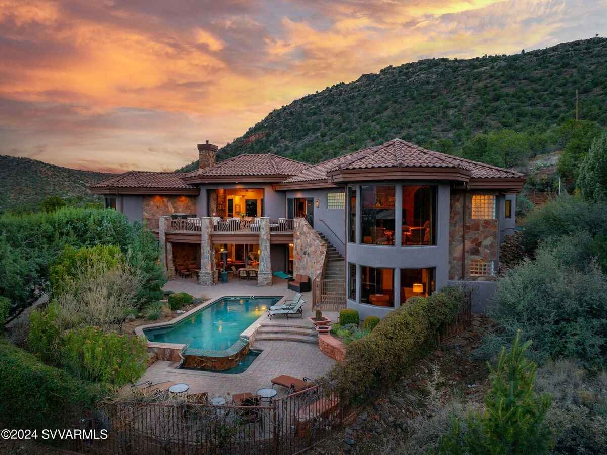 Rear exterior view of the house with a pool, landscaped yard, and multi-level design at sunset.