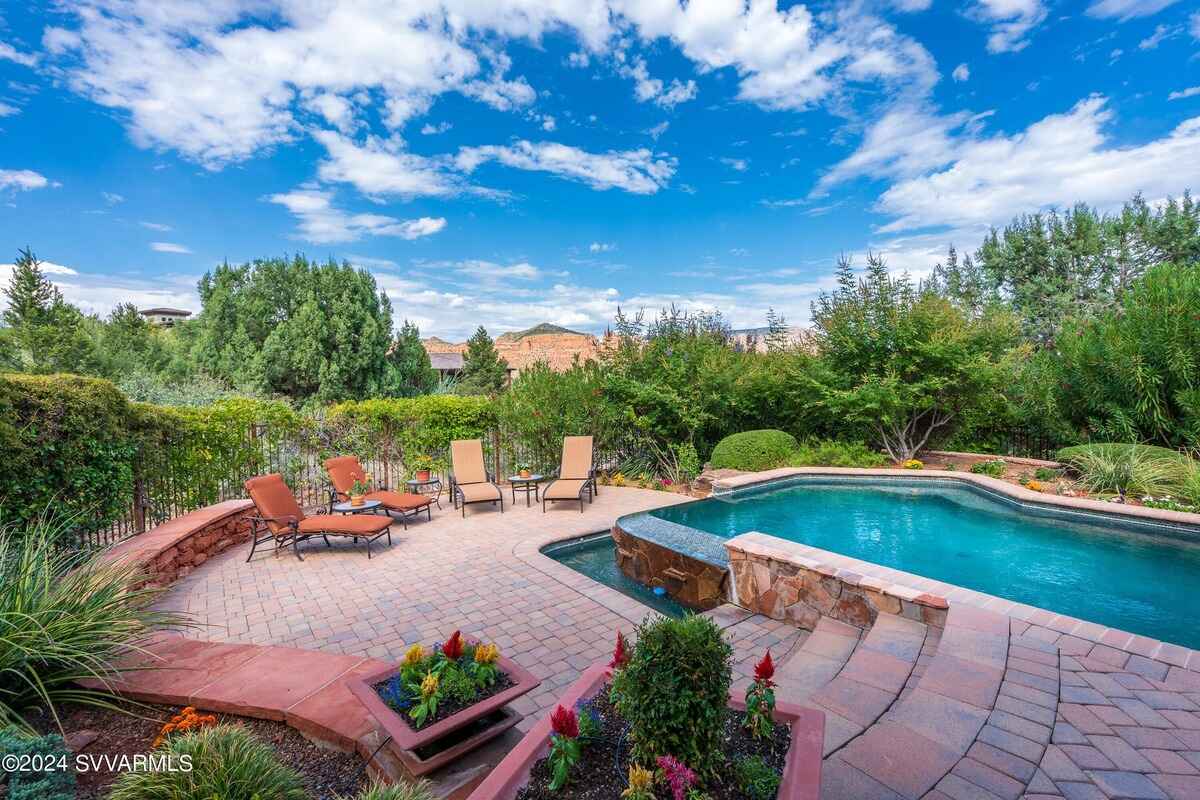 A backyard pool surrounded by brick pavers, lounge chairs, and landscaped greenery.