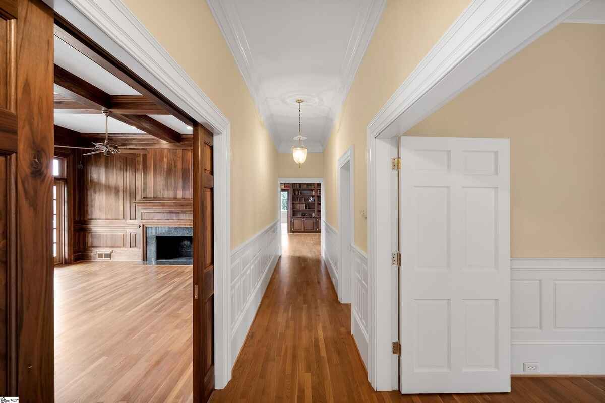 Hallway with detailed wainscoting leading to a room featuring built-in shelving.