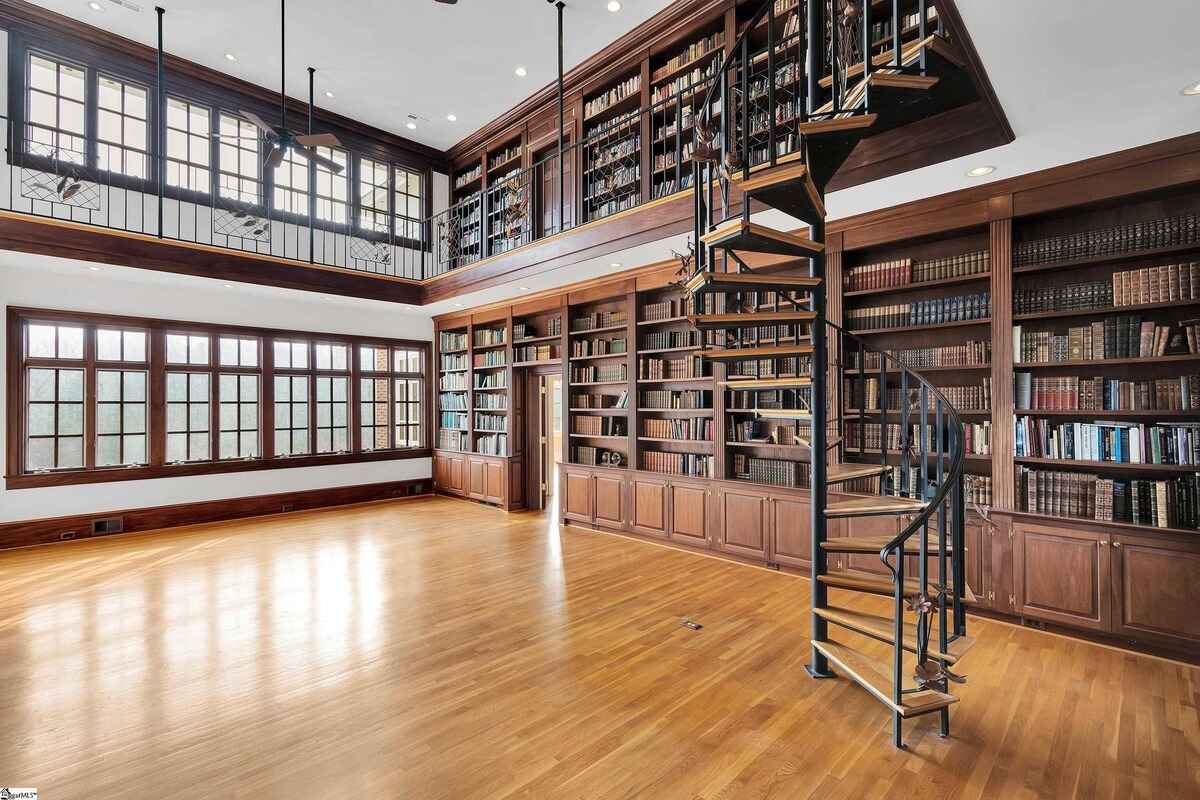 Two-story library with wooden bookshelves, a spiral staircase, and large windows.