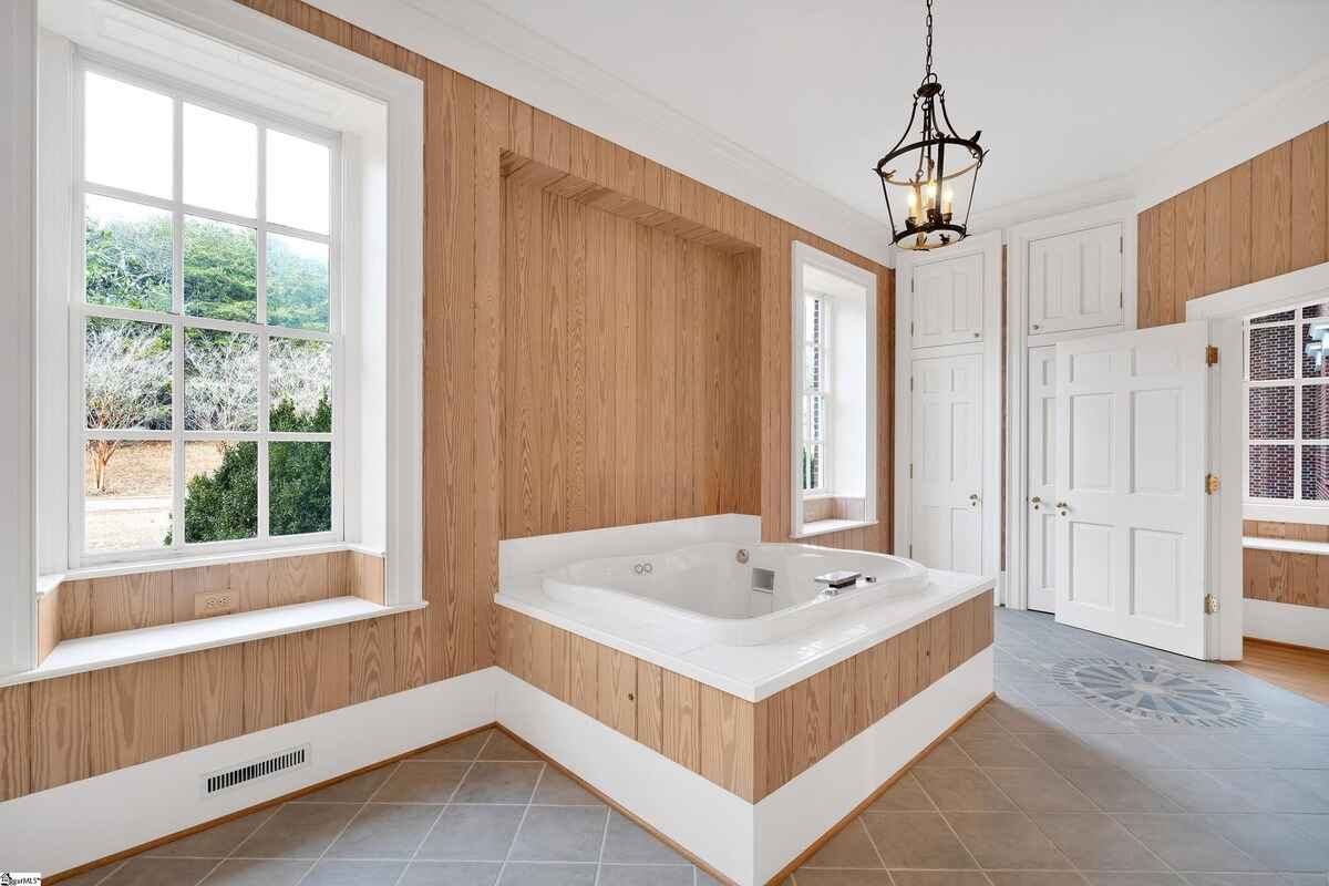 Bathroom with wood paneling, a corner tub, and large windows providing outside views.