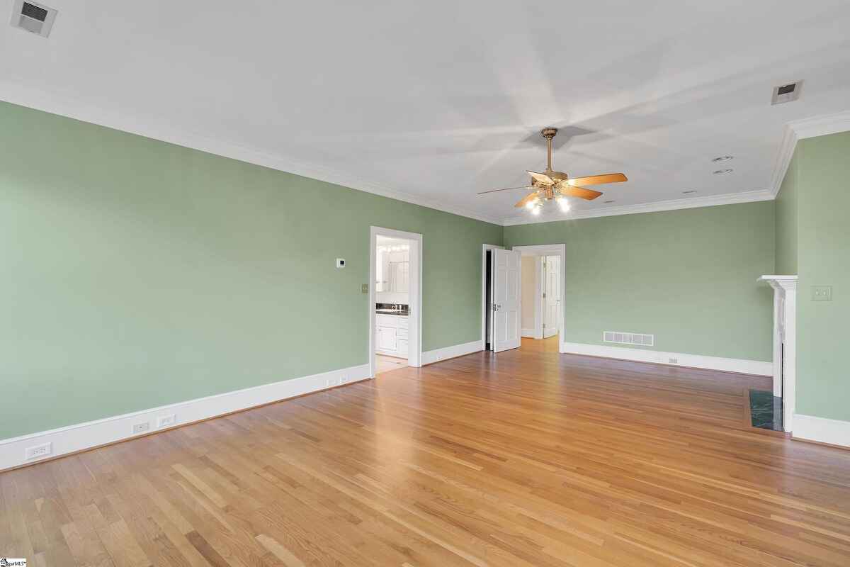 Spacious green-painted bedroom with ceiling fan and hardwood flooring.