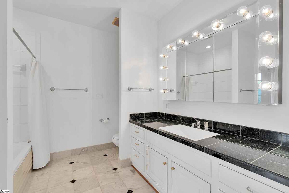 Bathroom with double vanity, black marble countertop, and lighted mirror.