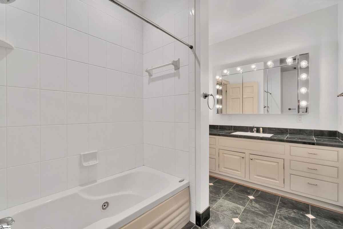 Bathroom with tiled shower and bathtub, marble vanity, and bright lighting.