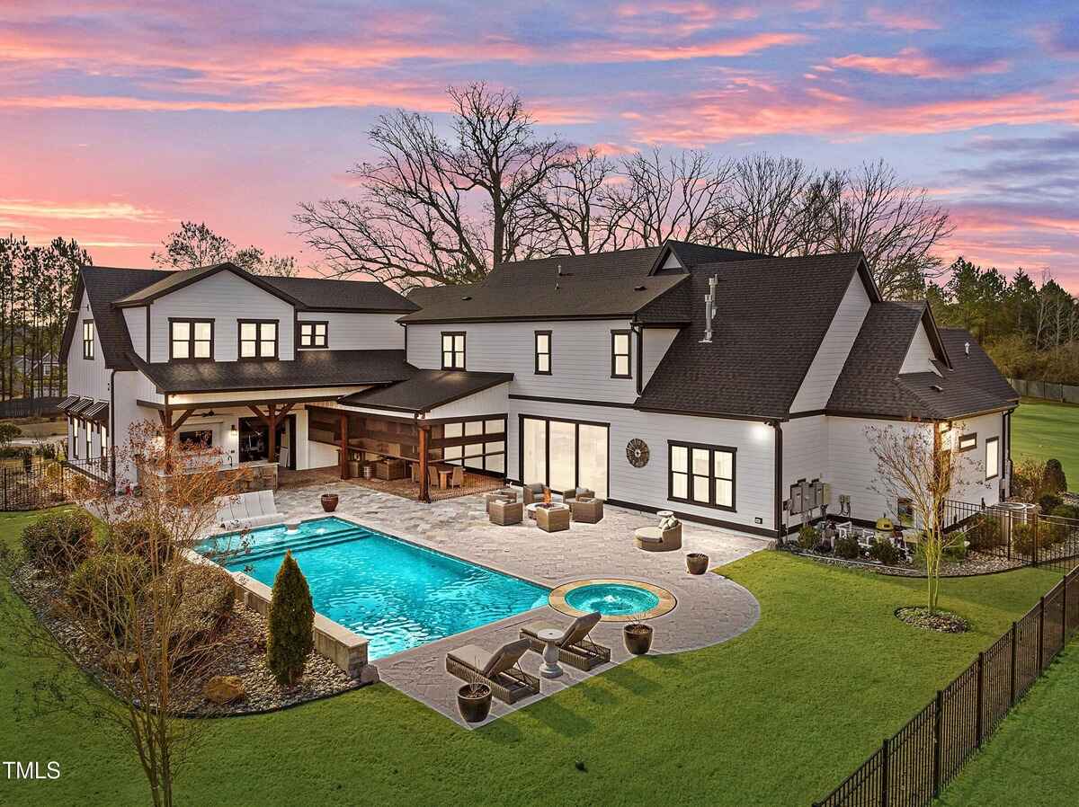 Expansive outdoor living area with pool, hot tub, and covered patio surrounded by manicured landscaping.