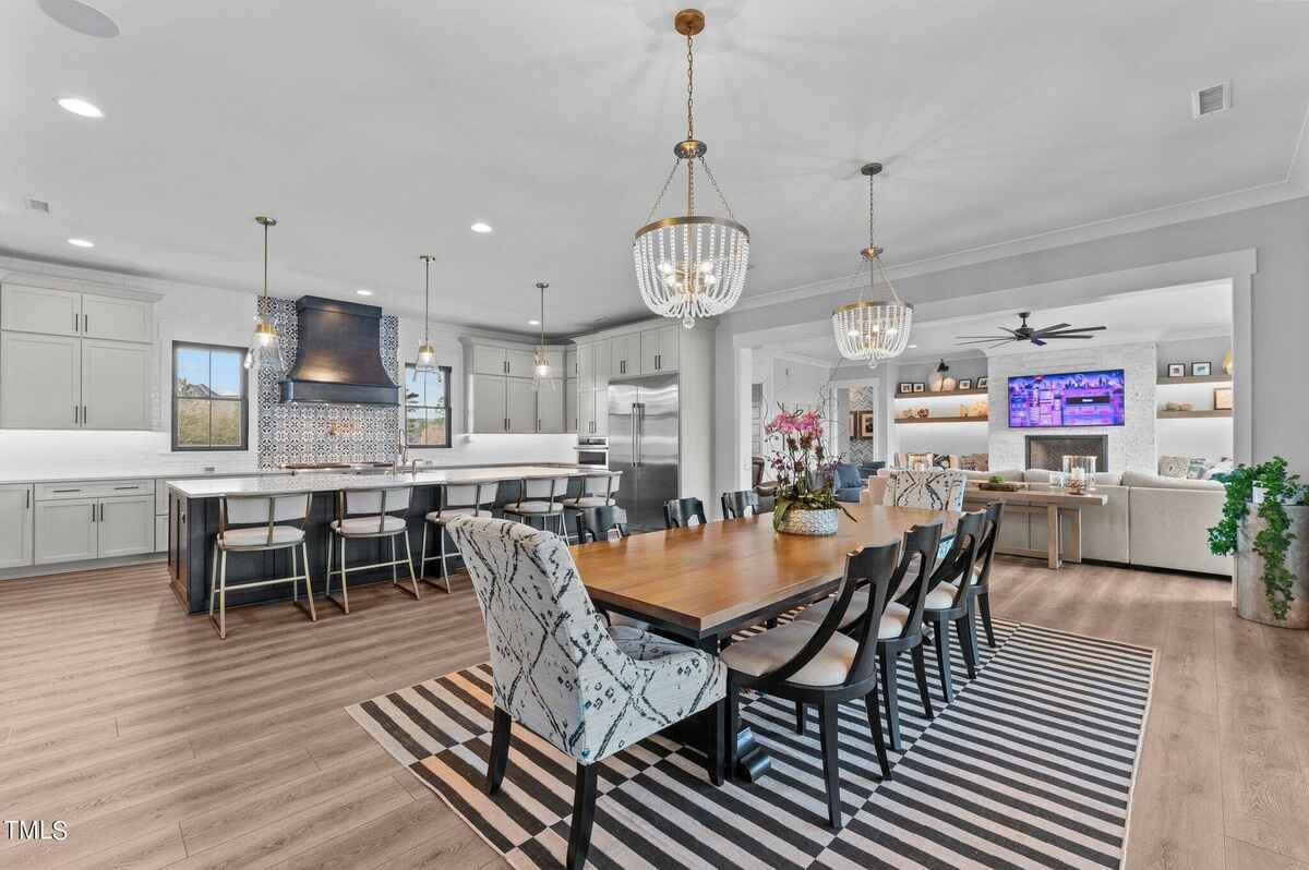 Open concept kitchen and dining area with a long table, chandeliers, and a view of the living room.