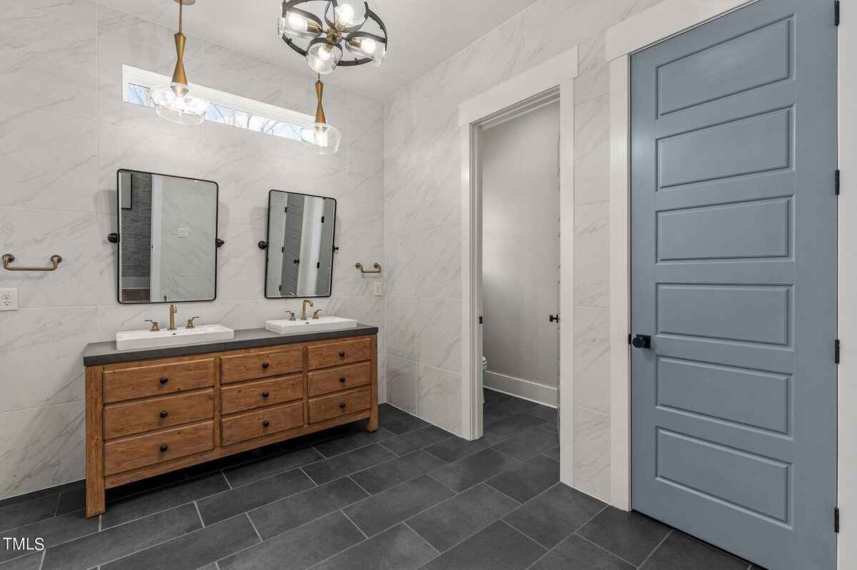 Double vanity bathroom with wooden cabinets, modern light fixtures, and tiled flooring.