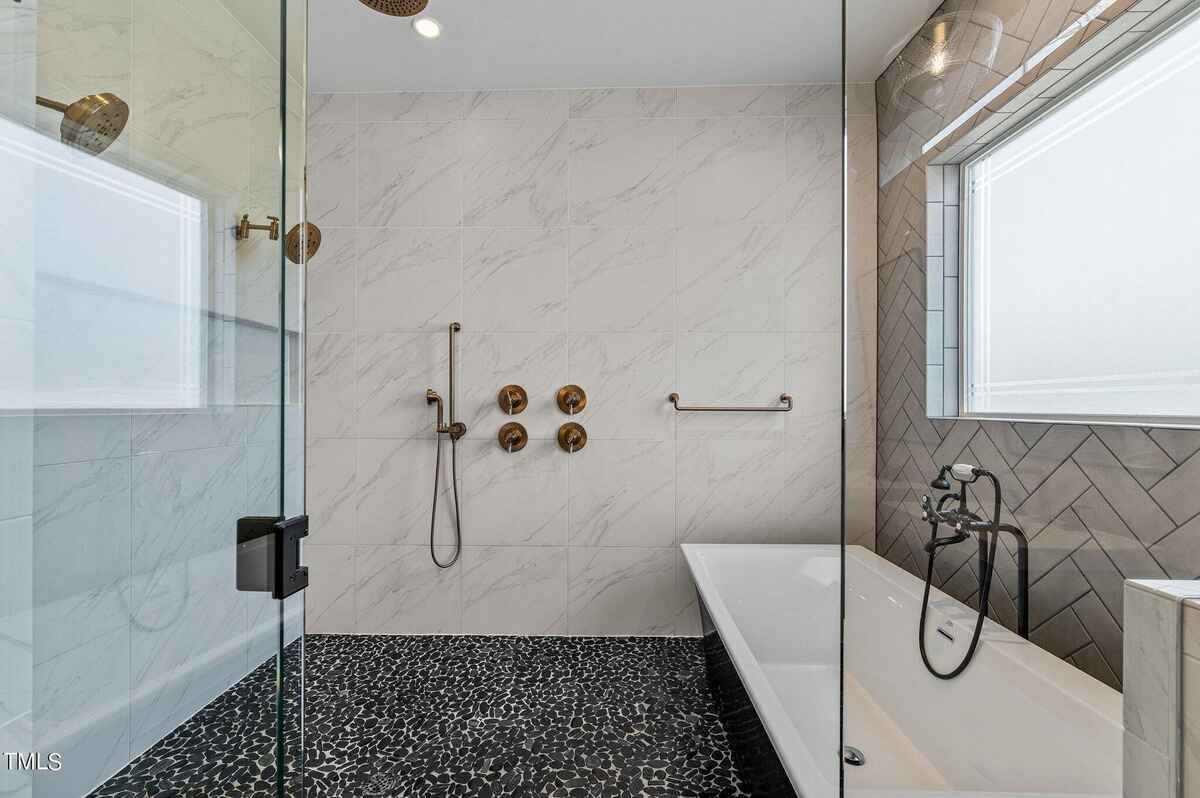 Walk-in shower with glass enclosure, marble tiles, and a freestanding bathtub.