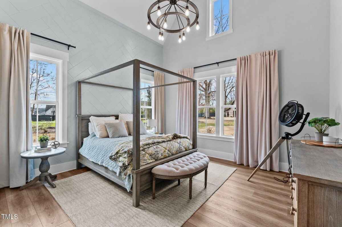 Bedroom with four-poster bed, light curtains, and a chandelier.