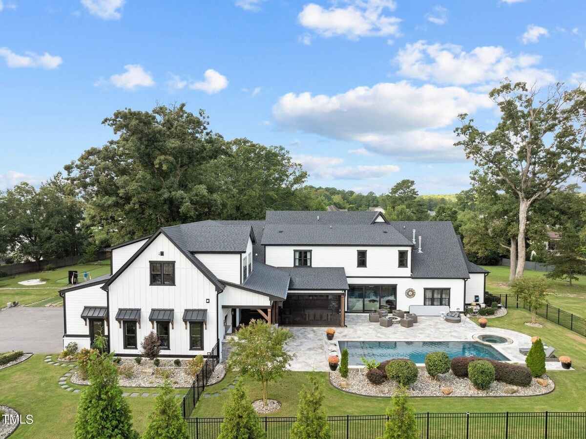 Large white farmhouse-style home with black accents, surrounded by lush greenery.