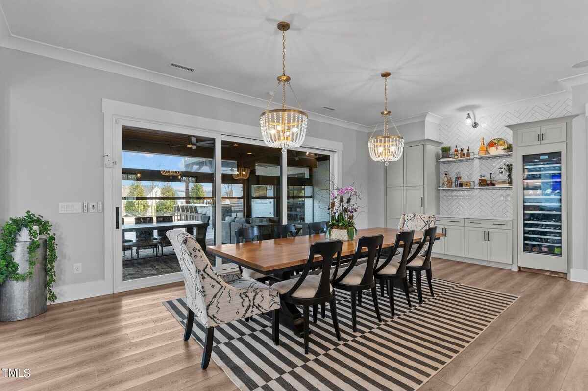 Dining room with long table, modern chandeliers, and view of outdoor space.