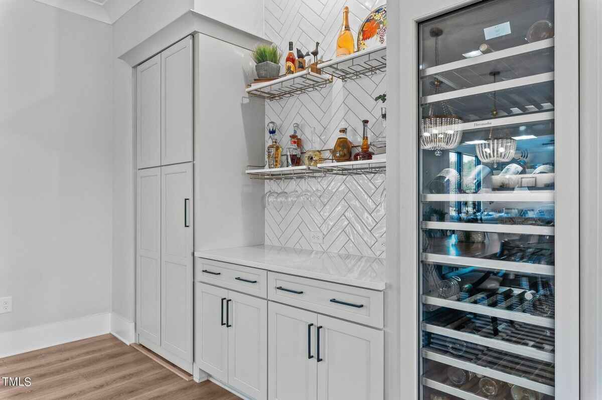 Bar area with built-in wine fridge, open shelving, and herringbone backsplash.