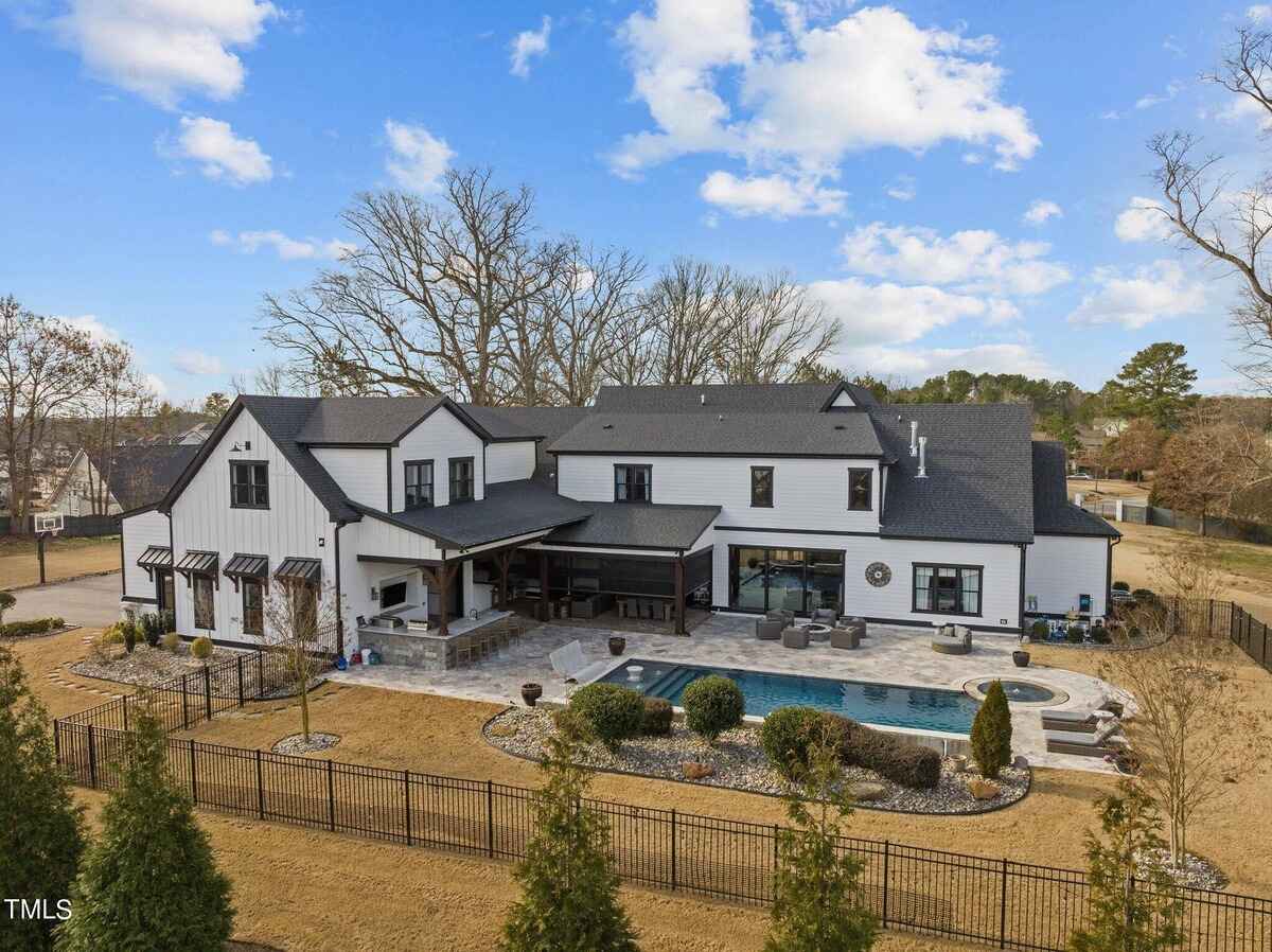 Large white house with black accents sits on a large grassy lot, with trees in the background.