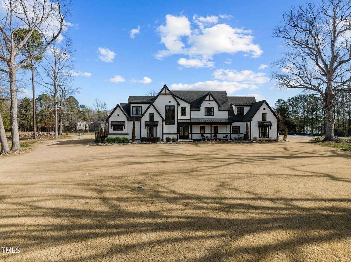 Large white farmhouse with black trim, a swimming pool, and outdoor patio area, is surrounded by a black metal fence.