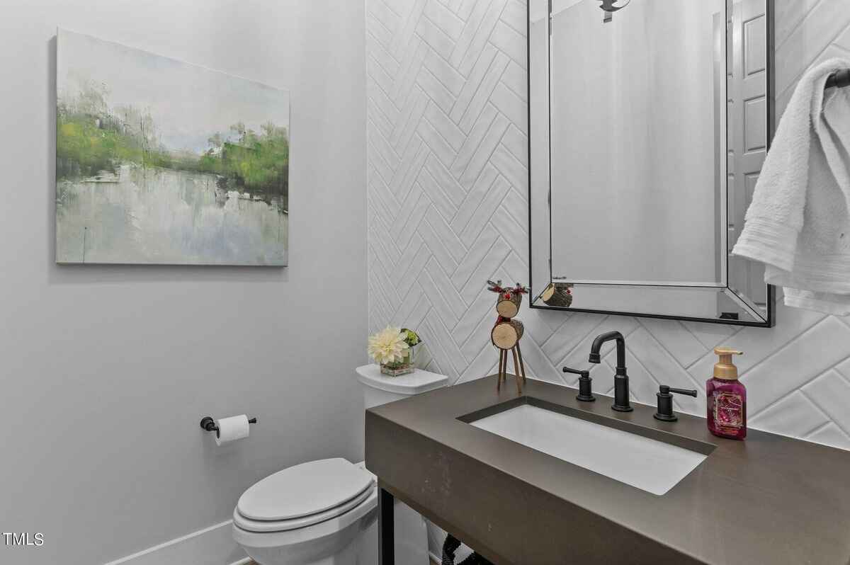 Powder room features a dark gray concrete vanity with a sink, white herringbone tile backsplash, and artwork above toilet.