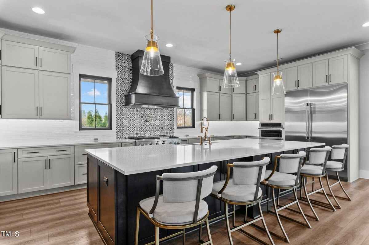 Kitchen features light gray cabinets, quartz countertops, a large island with bar stools, and a patterned backsplash.