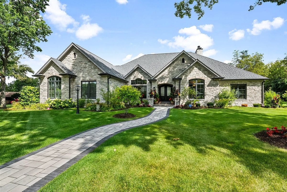 A winding stone path beckons you towards a grand residence, its facade a symphony of warm stone and elegant craftsmanship. 