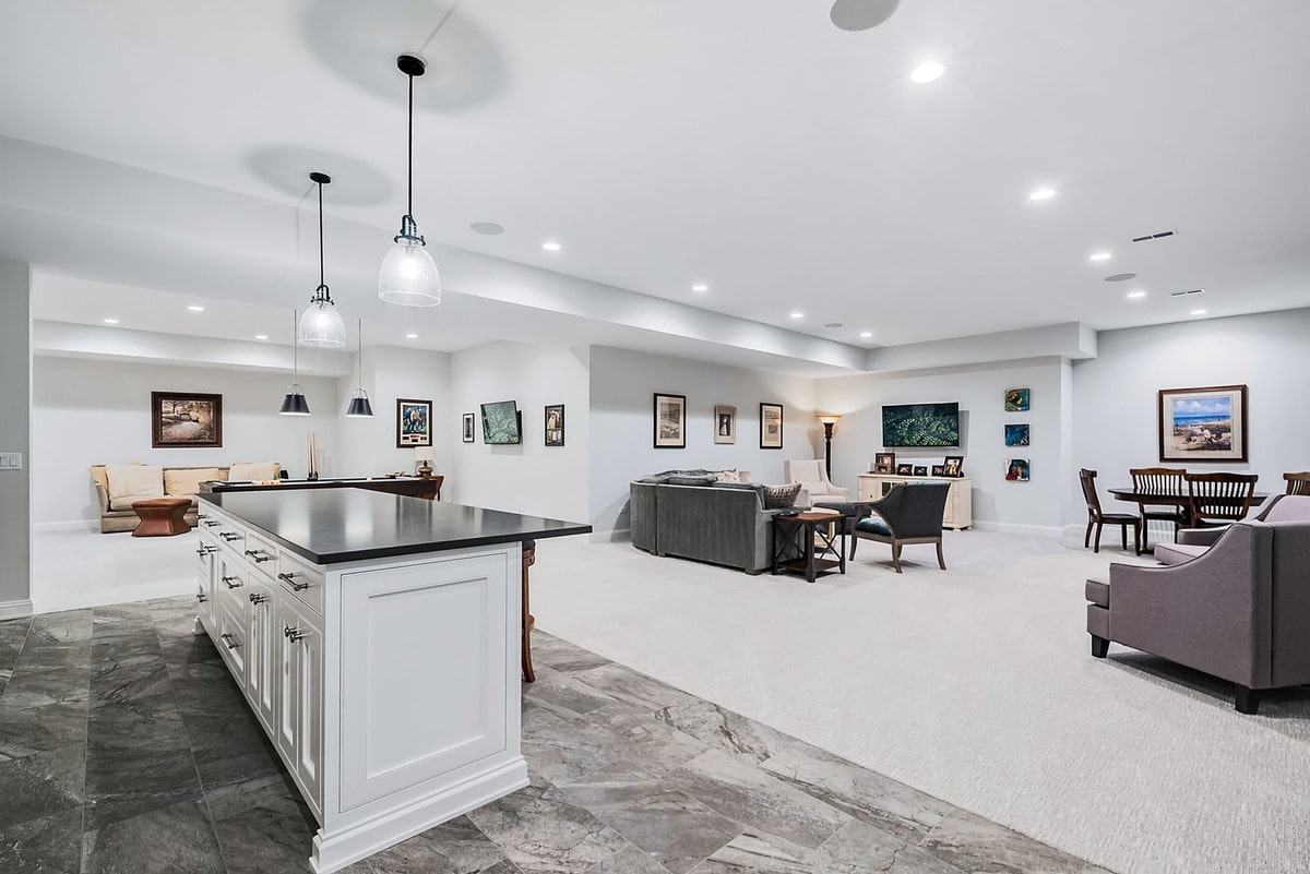 This open-concept basement space, bathed in natural light, showcases a seamless flow between the living room and kitchen. The grand scale of the room, accentuated by high ceilings and a statement chandelier, creates a welcoming and luxurious atmosphere.