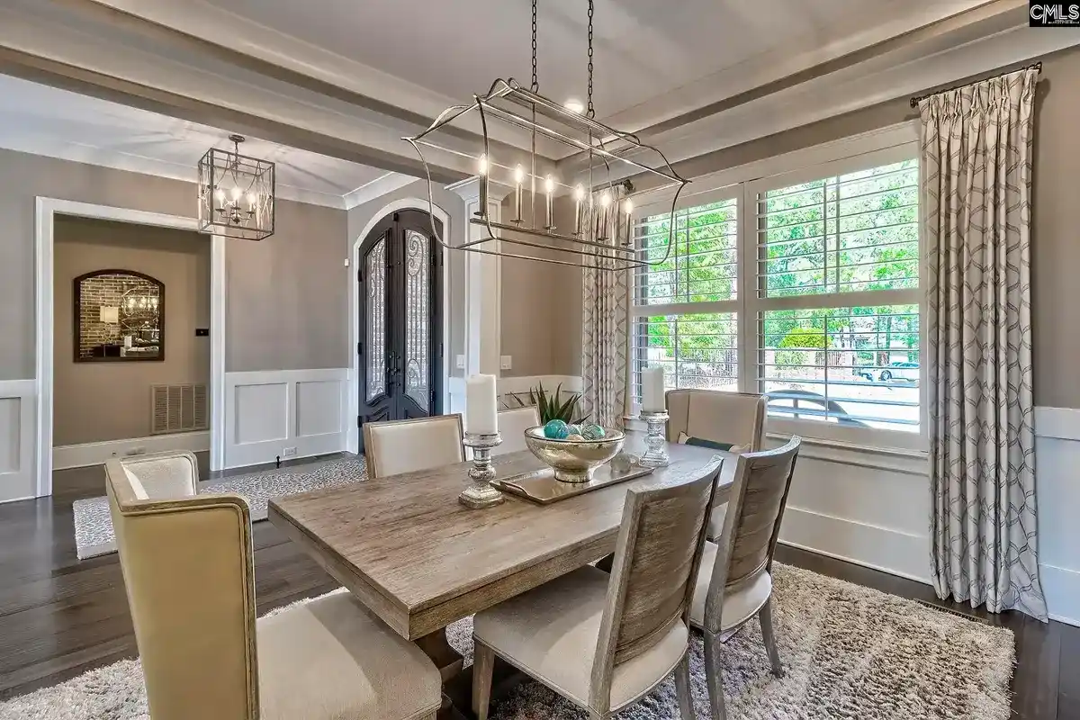 A formal dining room with a large wooden table, neutral-toned chairs, and a light gray and white color scheme is shown.