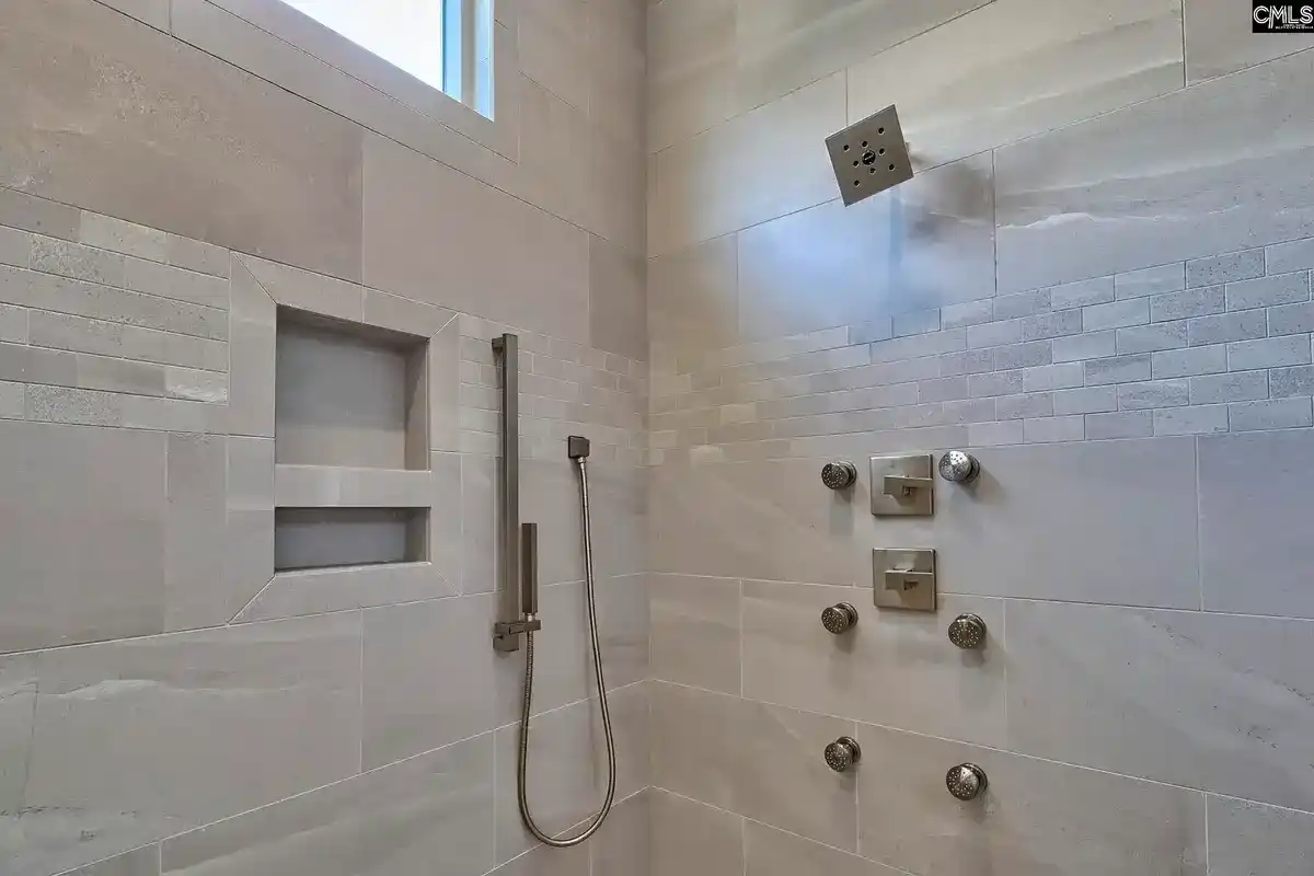 A modern shower with light-colored tile features multiple shower heads and built-in shelves.