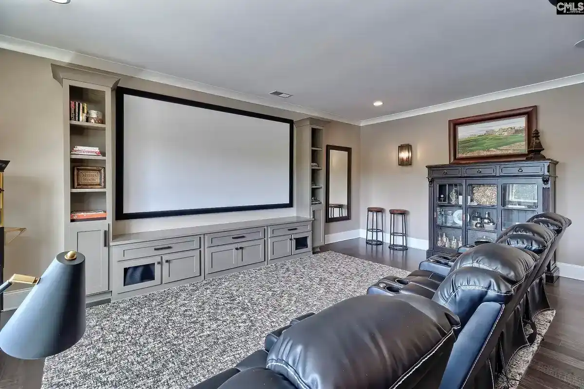 A home theater with a large projection screen, built-in shelving, and a black leather reclining seating area features gray cabinets and a neutral color scheme.