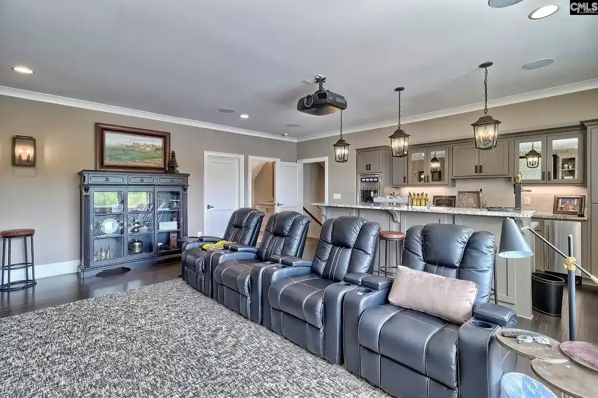 A home theater with three reclining chairs and a wet bar features gray cabinets, pendant lighting, and a neutral color scheme.