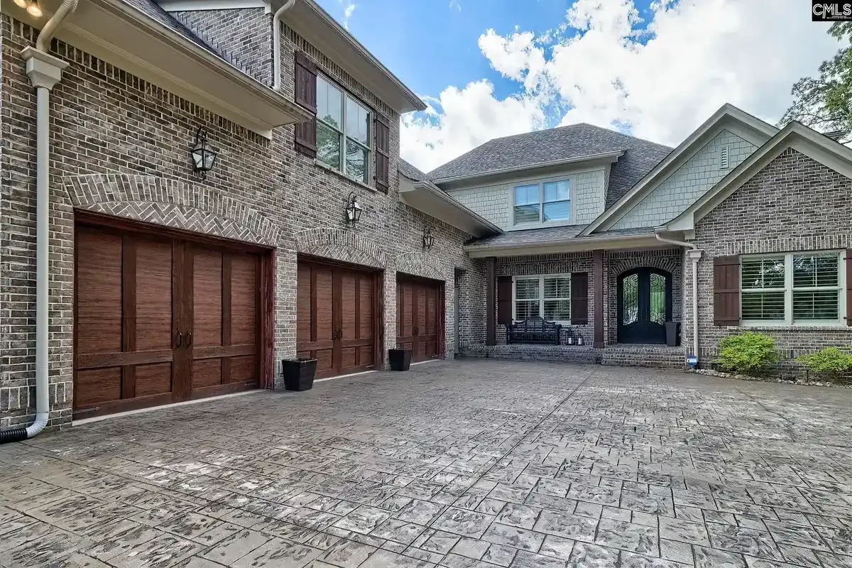 A large brick house with a three-car garage and a large stamped concrete driveway is shown in this photo.