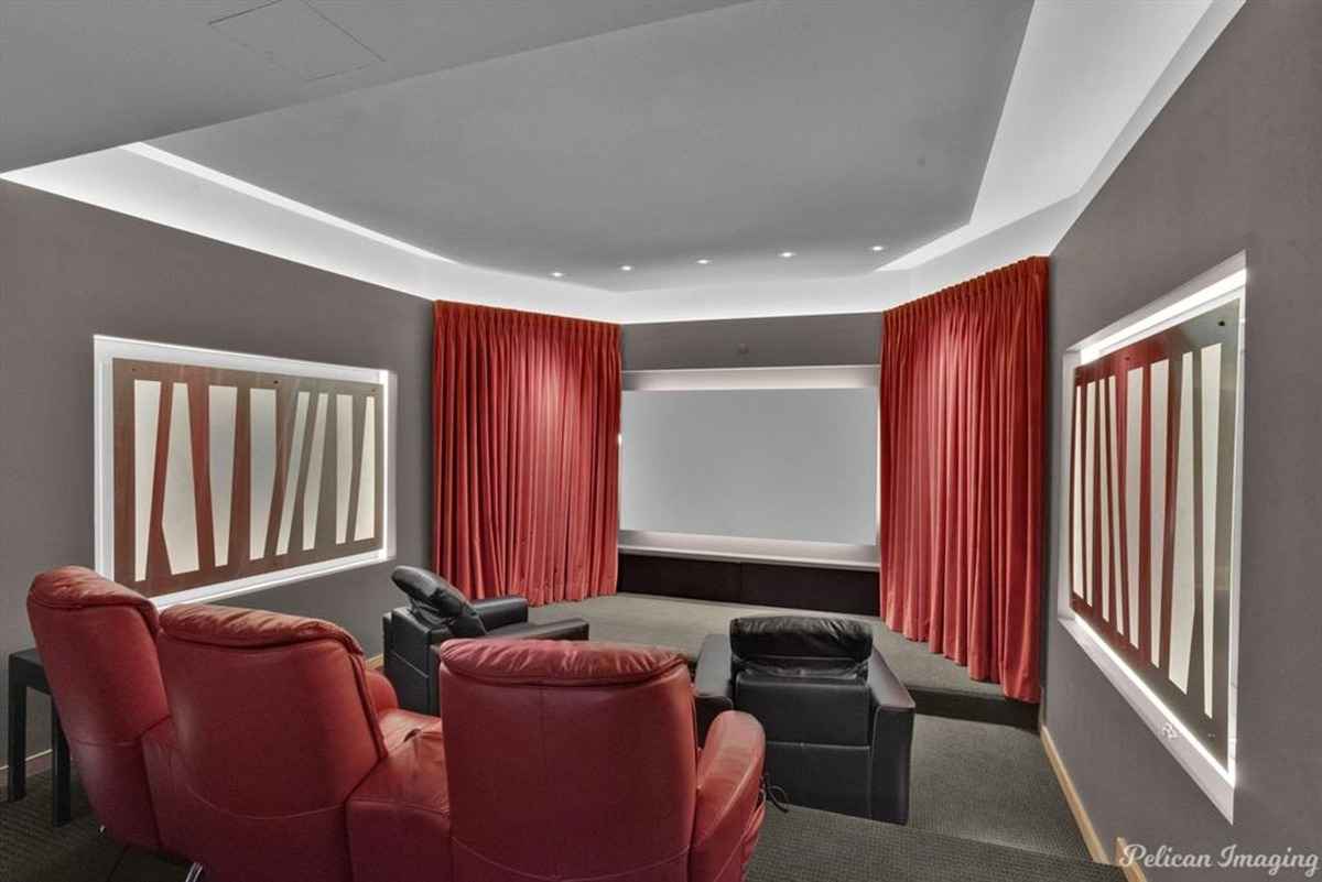 A private theater with recliner chairs, red curtains, and a large screen.