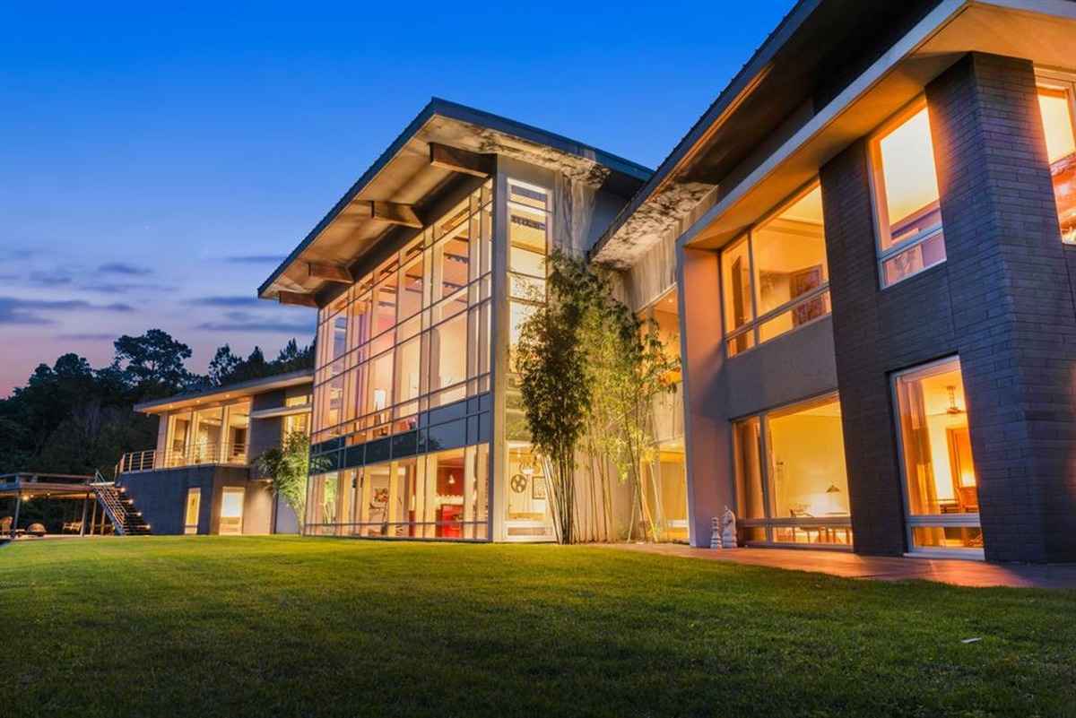 A stunning evening exterior of a modern home with large glass windows glowing warmly, surrounded by a well-manicured lawn.