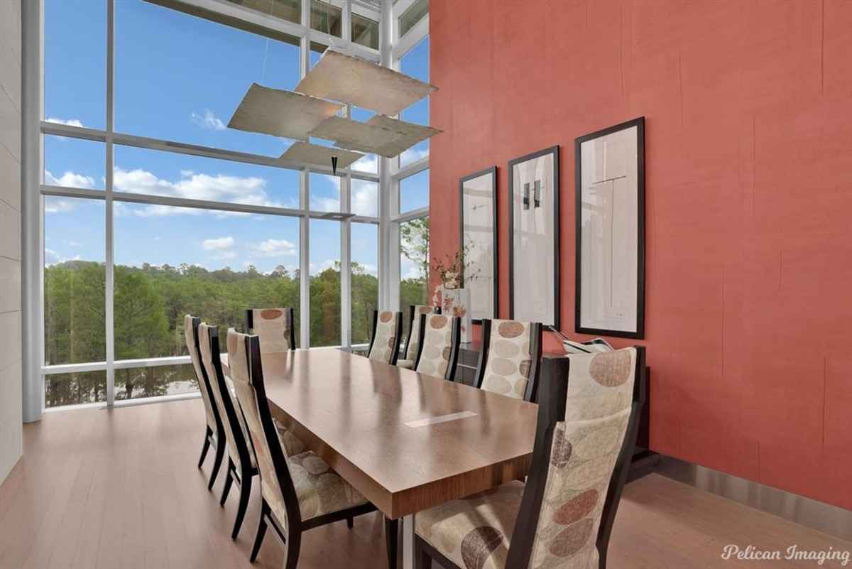 A modern dining room with a large wooden table, stylish chairs, and floor-to-ceiling windows offering scenic views.