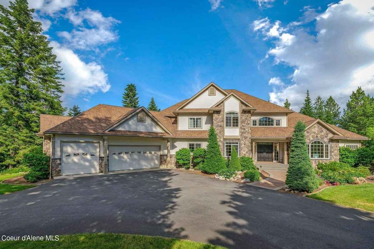 A large two-story house with stone accents and a three-car garage is shown in a sunny outdoor setting.