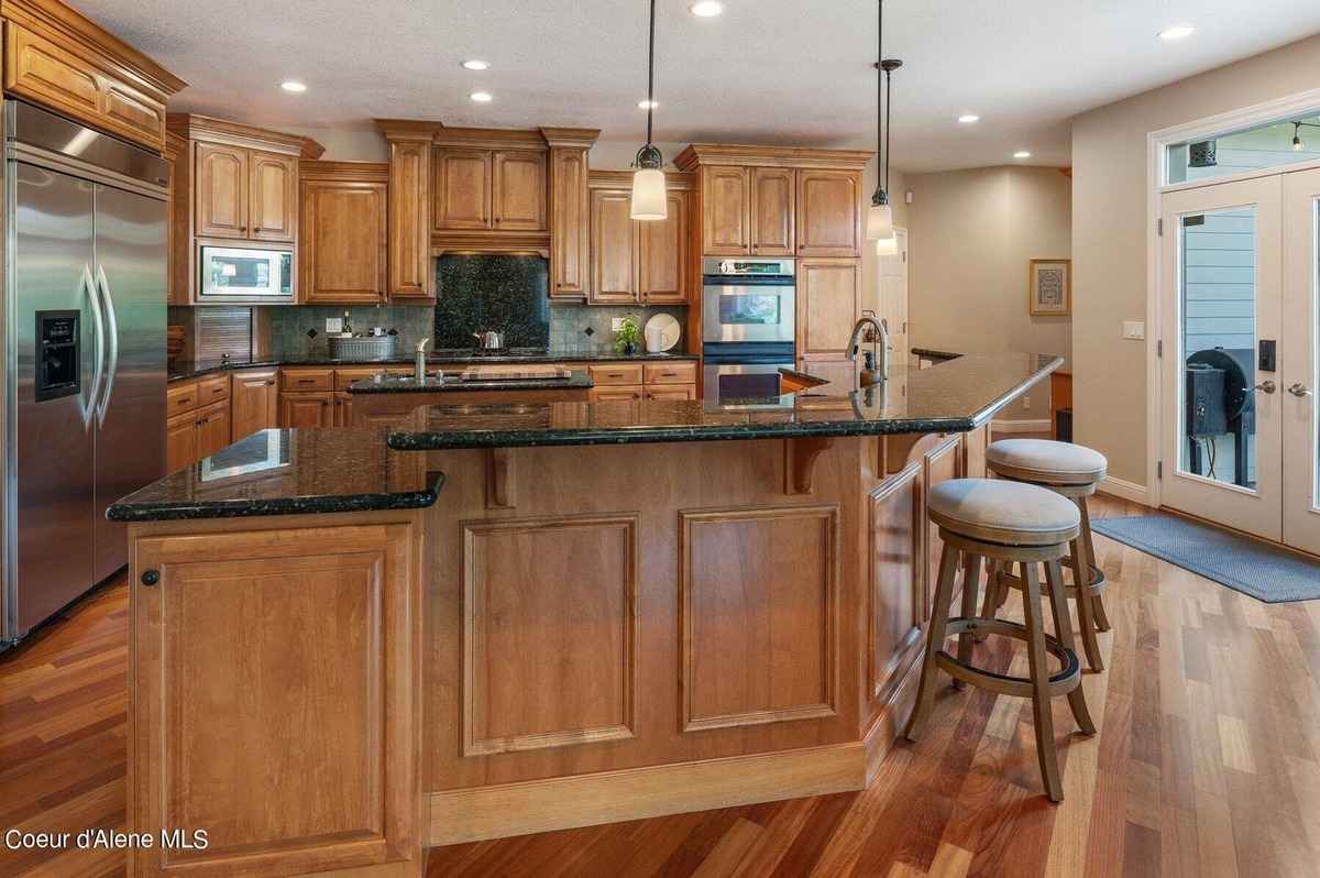 A kitchen with light wood cabinets, a large island with a dark countertop, and two wooden stools is shown.