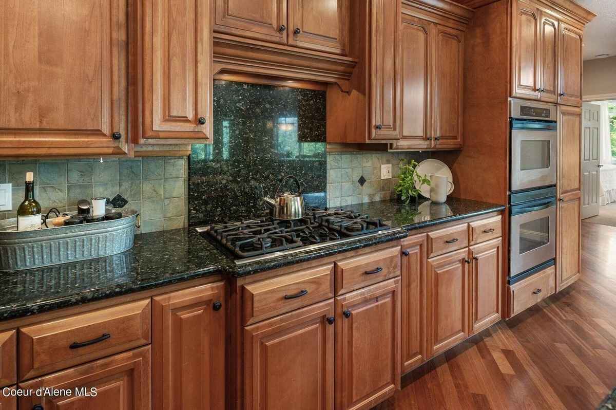 A kitchen features light brown wood cabinets, dark green granite countertops, and a gas stovetop.